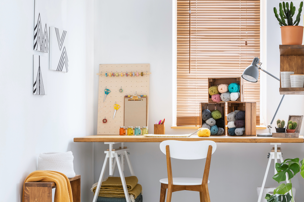Creative workspace with scandinavian, wooden furniture, white walls and sewing tools in a modern crafts room interior. Real photo.